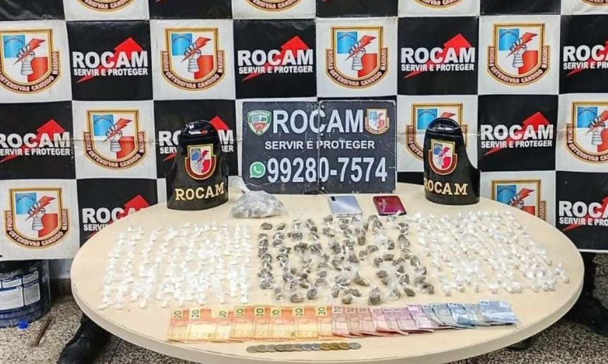 Apreensão de drogas: diversos pacotes e dinheiro sobre uma mesa, com emblemas da Rocam ao fundo.