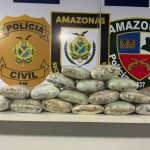 Apreensão de drogas pela polícia no Amazonas. Pacotes embalados em cima de uma mesa, com distintivos da polícia no fundo.