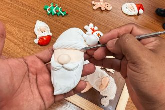 Artesão esculpindo detalhes em um enfeite de Natal de biscuit.