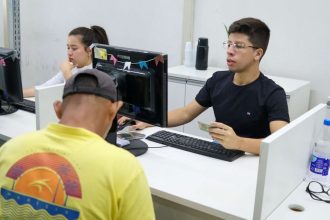 Atendimento em posto de emprego (Sine), com funcionário e cliente interagindo.