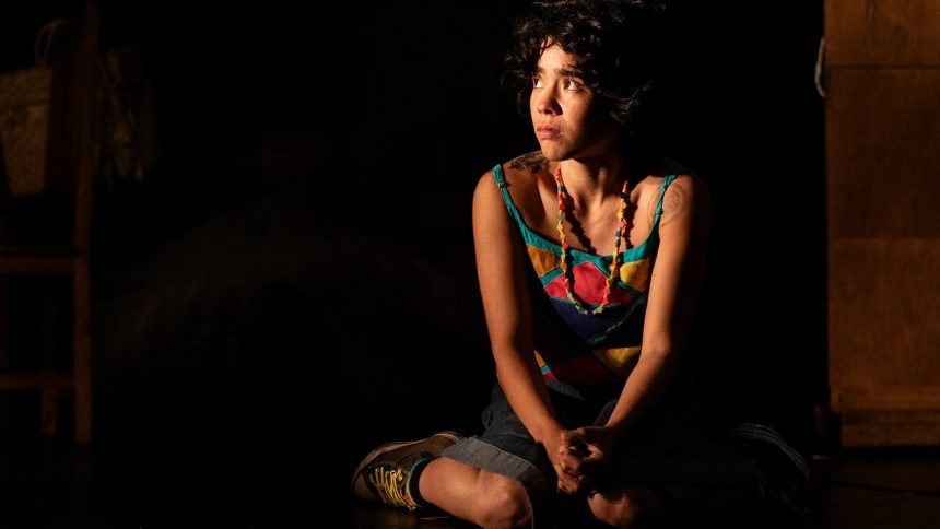 Atriz sentada com roupa colorida e colar em cena da peça 'Eu Capitu'