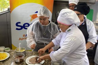 Aula de gastronomia com pessoas em uniformes de chef preparando alimentos, com ingredientes na bancada.