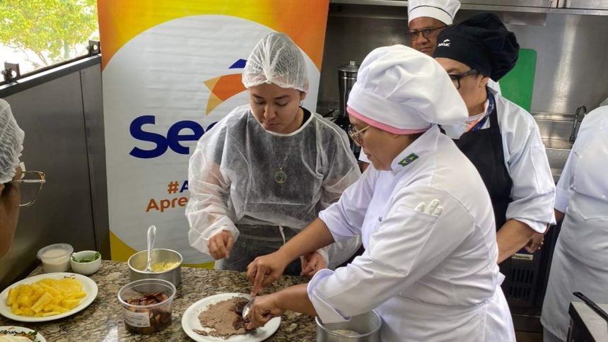 Aula de gastronomia com pessoas em uniformes de chef preparando alimentos, com ingredientes na bancada.