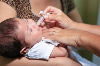 Bebê recebendo vacina oral em campanha de vacinação em UBS.