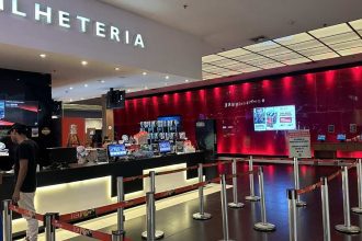 Bilheteria de cinema com letreiro 'BILHETERIA' e fila para atendimento.