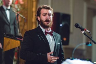 Cantor de terno e gravata borboleta se apresenta com microfone.