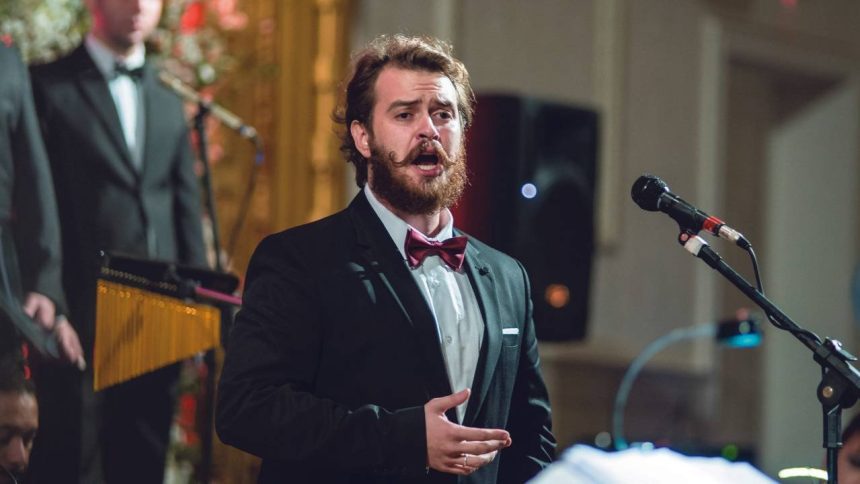 Cantor de terno e gravata borboleta se apresenta com microfone.