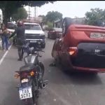Carro capotado na rua após acidente com roda solta. Motocicleta e pessoas ao redor.