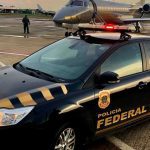 Carro da Polícia Federal em ação no aeroporto com avião ao fundo