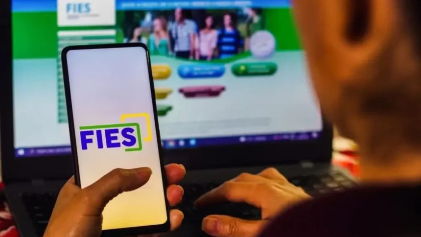 Celular com logo FIES e pessoa usando notebook