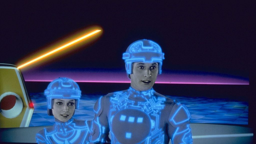 Cena do filme Tron com dois personagens em trajes futuristas e luzes neon.