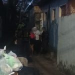 Cena noturna em beco, com pessoas e sacos de lixo.