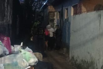 Cena noturna em beco, com pessoas e sacos de lixo.