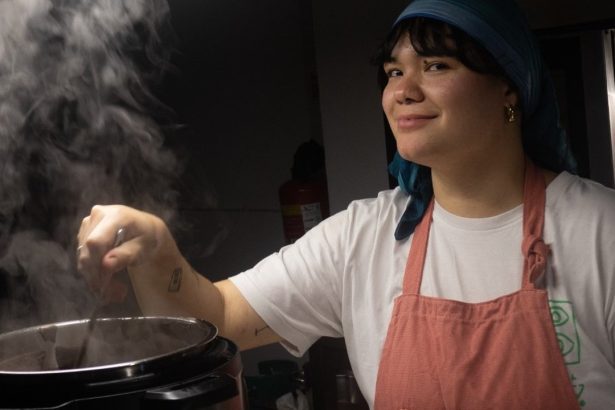 Chef paraense sorrindo enquanto cozinha, com vapor subindo de uma panela.