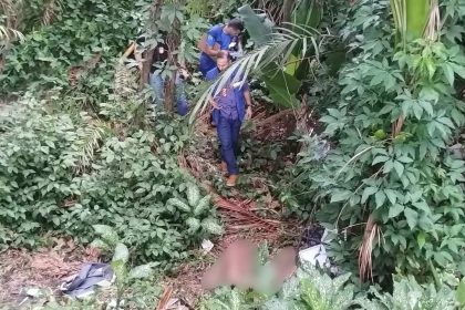 Corpo de homem sem roupa encontrado em mata, com policiais no local.