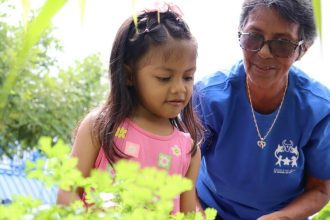 Criança e idosa em projeto social, com plantas ao fundo.