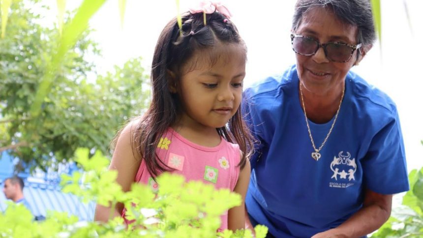 Criança e idosa em projeto social, com plantas ao fundo.