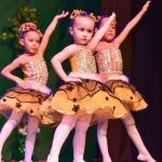 Crianças em figurino de bailarinas, apresentando-se em um palco decorado com tema floral.