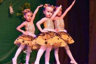 Crianças em figurino de bailarinas, apresentando-se em um palco decorado com tema floral.