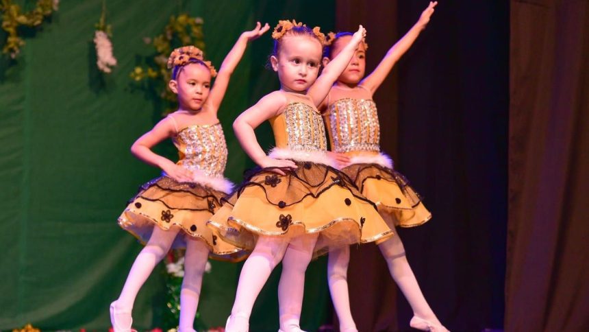 Crianças em figurino de bailarinas, apresentando-se em um palco decorado com tema floral.