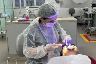 Dentista realizando procedimento odontológico em paciente, usando equipamento e vestindo equipamentos de proteção.