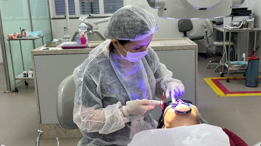 Dentista realizando procedimento odontológico em paciente, usando equipamento e vestindo equipamentos de proteção.