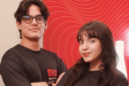 Dois jovens sorrindo em frente a um fundo vermelho com linhas curvas.