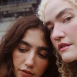 Duas mulheres juntas, uma com cabelo castanho e outra loira, com um fundo desfocado.