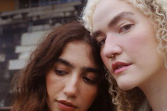 Duas mulheres juntas, uma com cabelo castanho e outra loira, com um fundo desfocado.