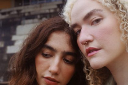 Duas mulheres juntas, uma com cabelo castanho e outra loira, com um fundo desfocado.