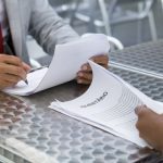 Duas pessoas analisando documentos de inventário em um escritório.