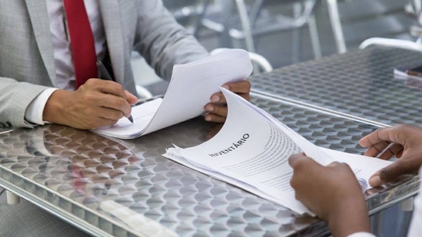 Duas pessoas analisando documentos de inventário em um escritório.