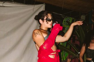 Duca Vieira cantando no palco com roupa vermelha e óculos escuros