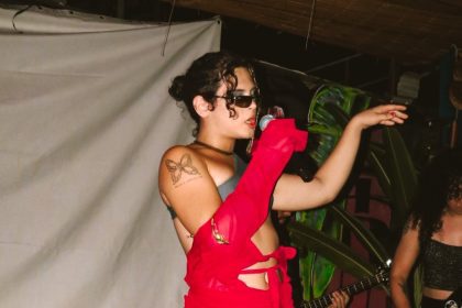 Duca Vieira cantando no palco com roupa vermelha e óculos escuros
