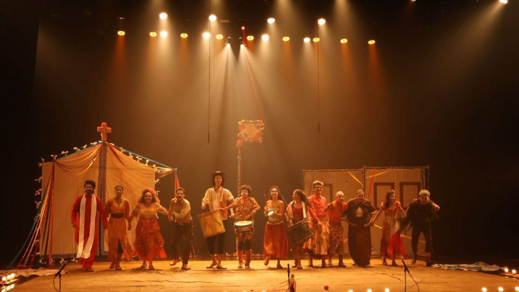 Elenco em palco do Festival de Teatro da Amazônia, com figurinos coloridos e iluminação teatral.