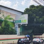 Fachada da ESBAM, escola com placa e carros estacionados na rua.