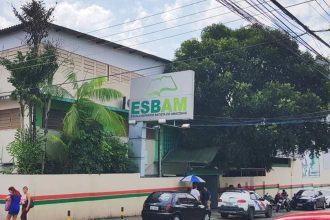 Fachada da ESBAM, escola com placa e carros estacionados na rua.