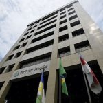 Fachada do TRT da 11ª Região, com bandeiras e céu azul.