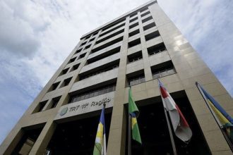 Fachada do TRT da 11ª Região, com bandeiras e céu azul.