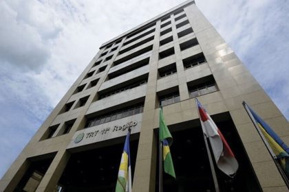 Fachada do TRT da 11ª Região, com bandeiras e céu azul.