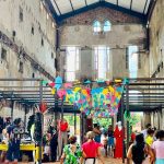 Feira criativa Caipora com pessoas e expositores em espaço com arquitetura antiga.