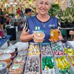 Feira de produtos regionais em Manaus, com vendedora sorrindo e mostrando seus produtos.