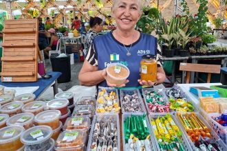 Feira de produtos regionais em Manaus, com vendedora sorrindo e mostrando seus produtos.