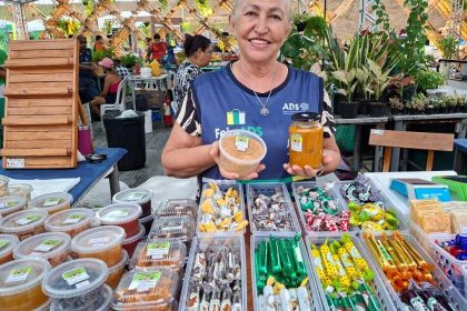 Feira de produtos regionais em Manaus, com vendedora sorrindo e mostrando seus produtos.