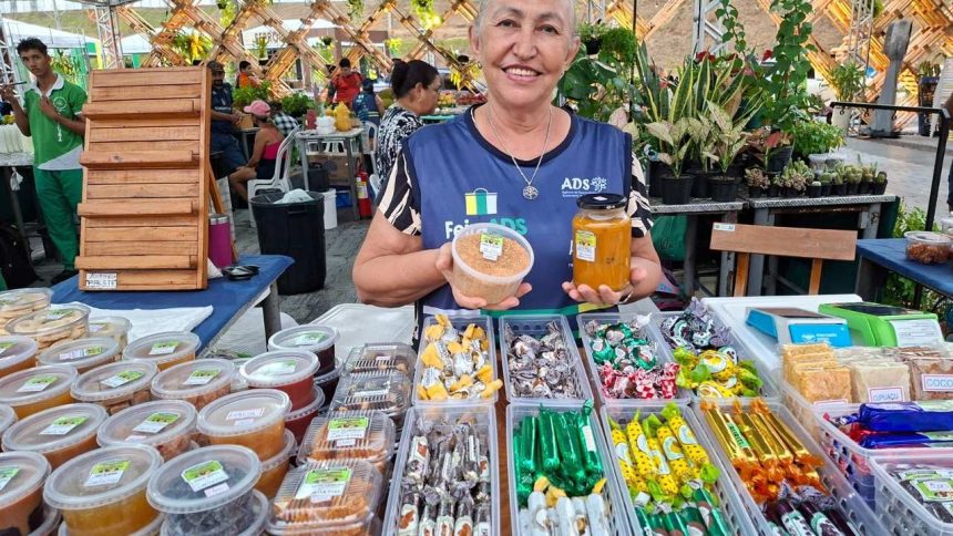 Feira de produtos regionais em Manaus, com vendedora sorrindo e mostrando seus produtos.