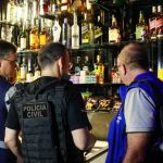 Fiscais em operação em estabelecimento, com bebidas alcoólicas em prateleiras.