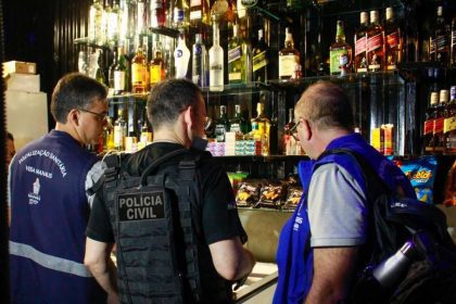 Fiscais em operação em estabelecimento, com bebidas alcoólicas em prateleiras.