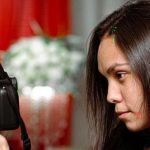 Fotógrafa segurando câmera EOS 400D, com detalhes em exposição sobre hip-hop amazonense.