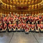 Grupo de artistas do 'Rei do Show' posando no Teatro Amazonas, com figurino vermelho.