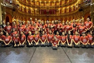 Grupo de artistas do 'Rei do Show' posando no Teatro Amazonas, com figurino vermelho.